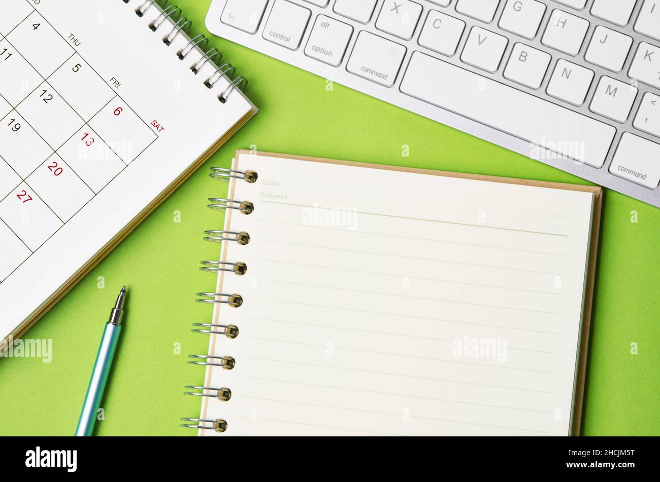 Open blank diary and desk calendar with computer keyboard on green background. Stock Photo