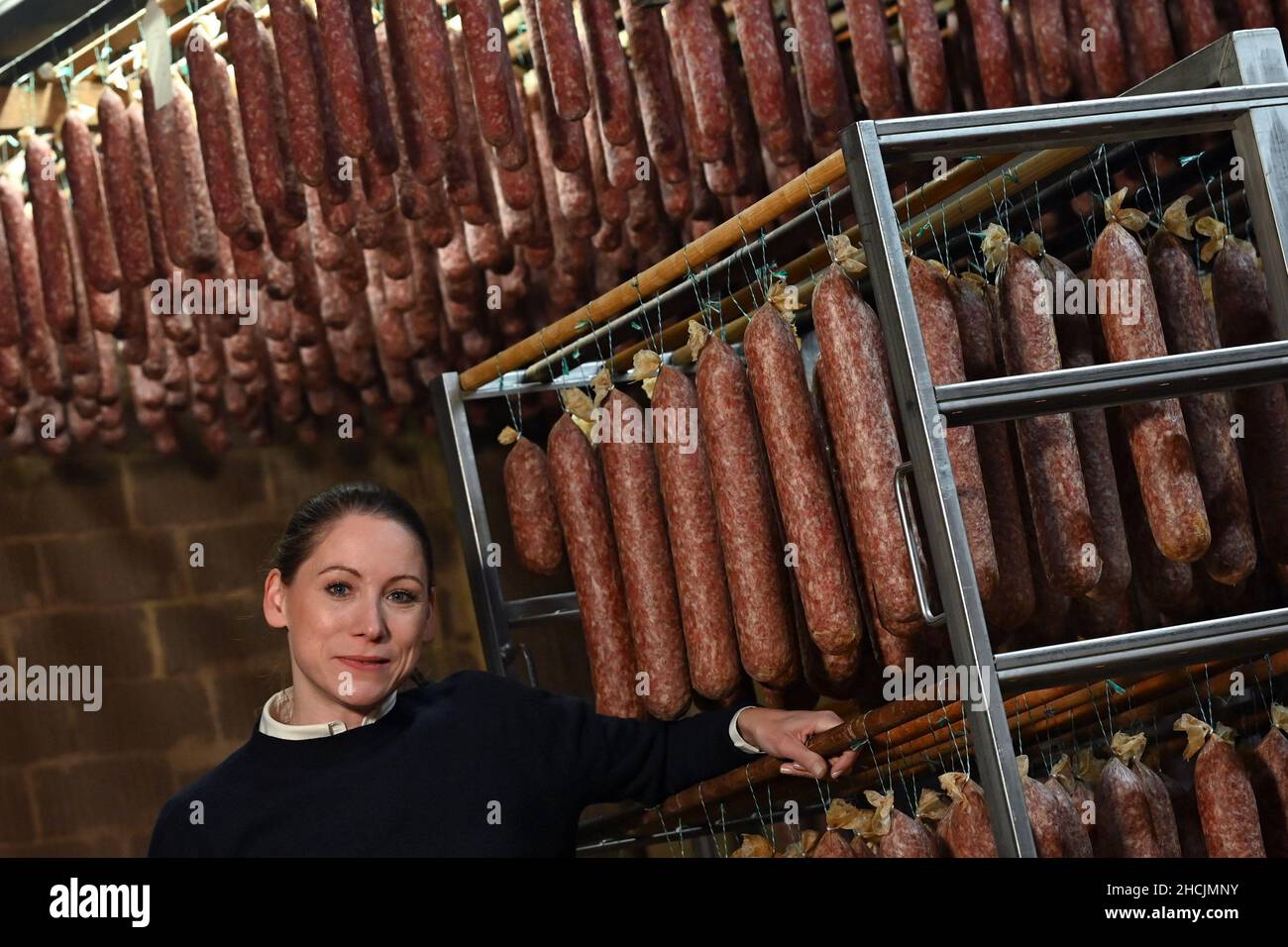 Calden, Germany. 27th Dec, 2021. Katharina Koch, Managing Director of Landfleischerei Henry Koch, stands next to 'Ahlen Würsten', a North Hessian sausage speciality. The company has been producing the air-dried mettwurst, which has its origins in the house slaughtering that used to be common, since 1877. The sausages mature for between four weeks and twelve months in the sausage heaven, a chamber surrounded by clay walls. (to dpa: 'Northern Hesse's 'Ahle Wurst': Cult object between tradition and innovation') Credit: Uwe Zucchi/dpa/Alamy Live News Stock Photo