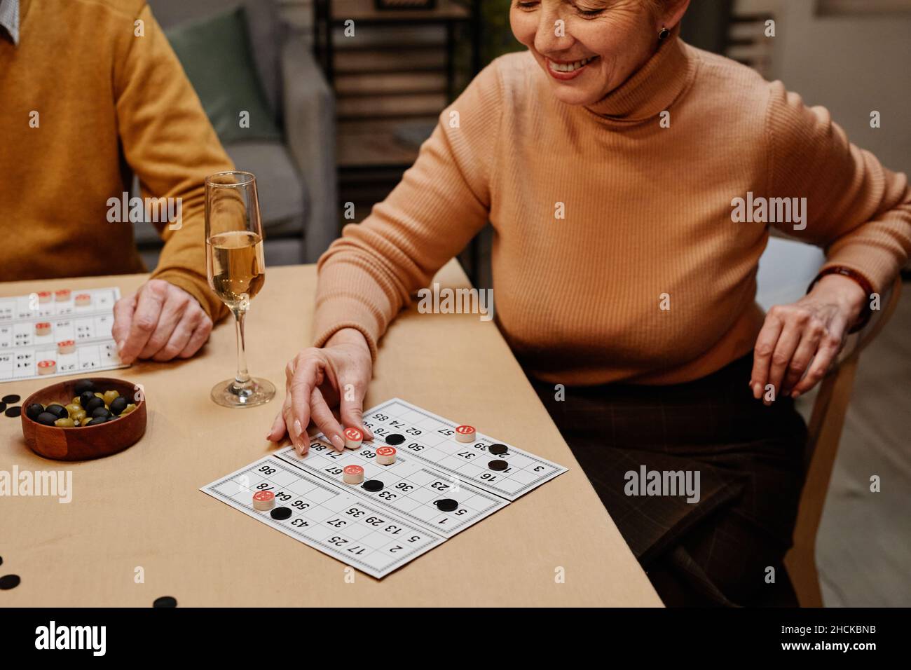 Beautiful aged Caucasian woman wearing casual clothes sitting at wooden table with snack and drinks and playing board game with friends Stock Photo