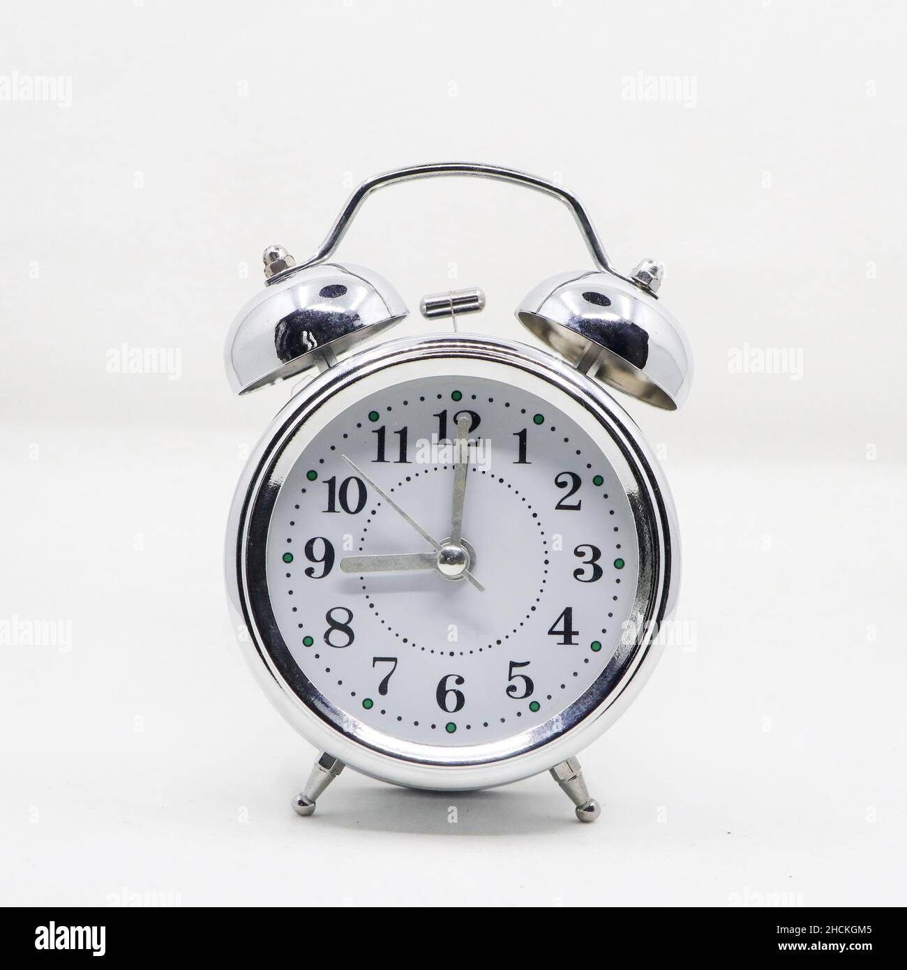 a vintage classic ringing alarm clock with a silver body and white analog round dial isolated in a white background Stock Photo