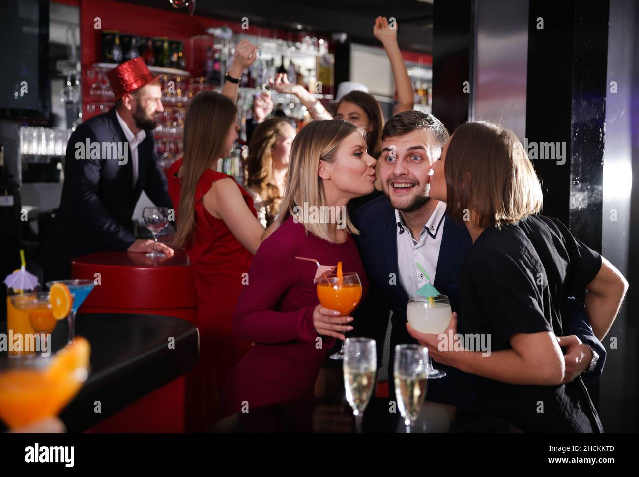 Guy getting friendly kiss by two girls in bar Stock Photo - Alamy