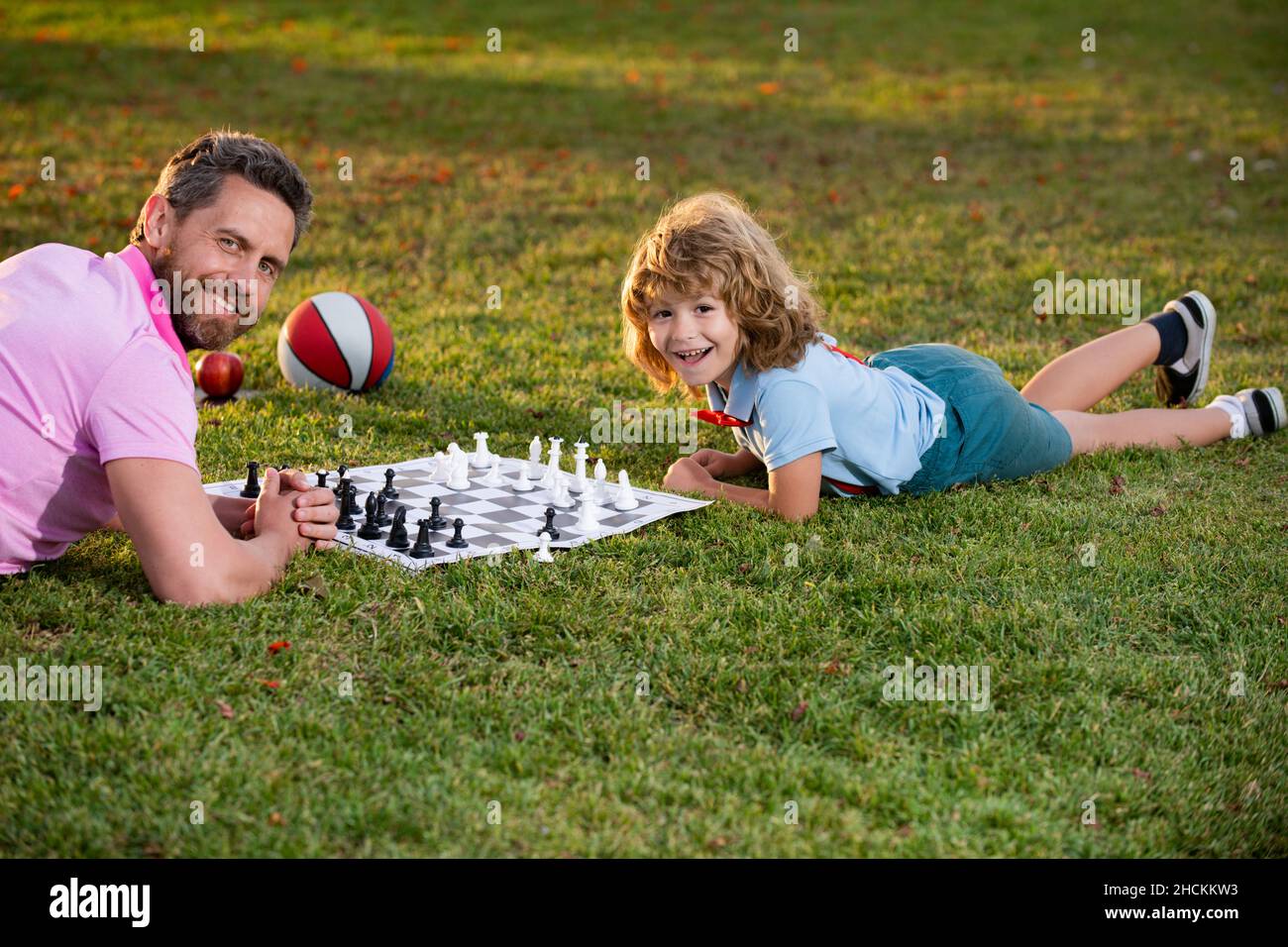 Happy family outdoor. Father and son playing chess in spring garden. Child learning to play chess. Little boy think or plan chess game. Checkmate. Stock Photo
