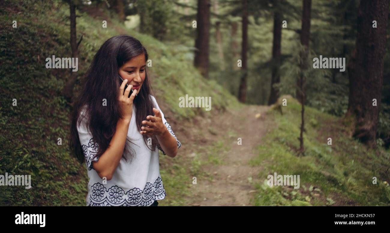 Young brunette Indian girl talking on the phone while standing in a ...