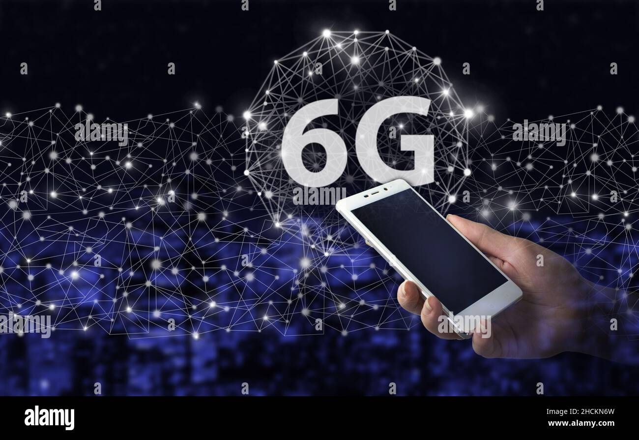 Wireless systems and internet of things IOT . Hand hold white smartphone with digital hologram 6G sign on city dark blurred background. Abstract world Stock Photo