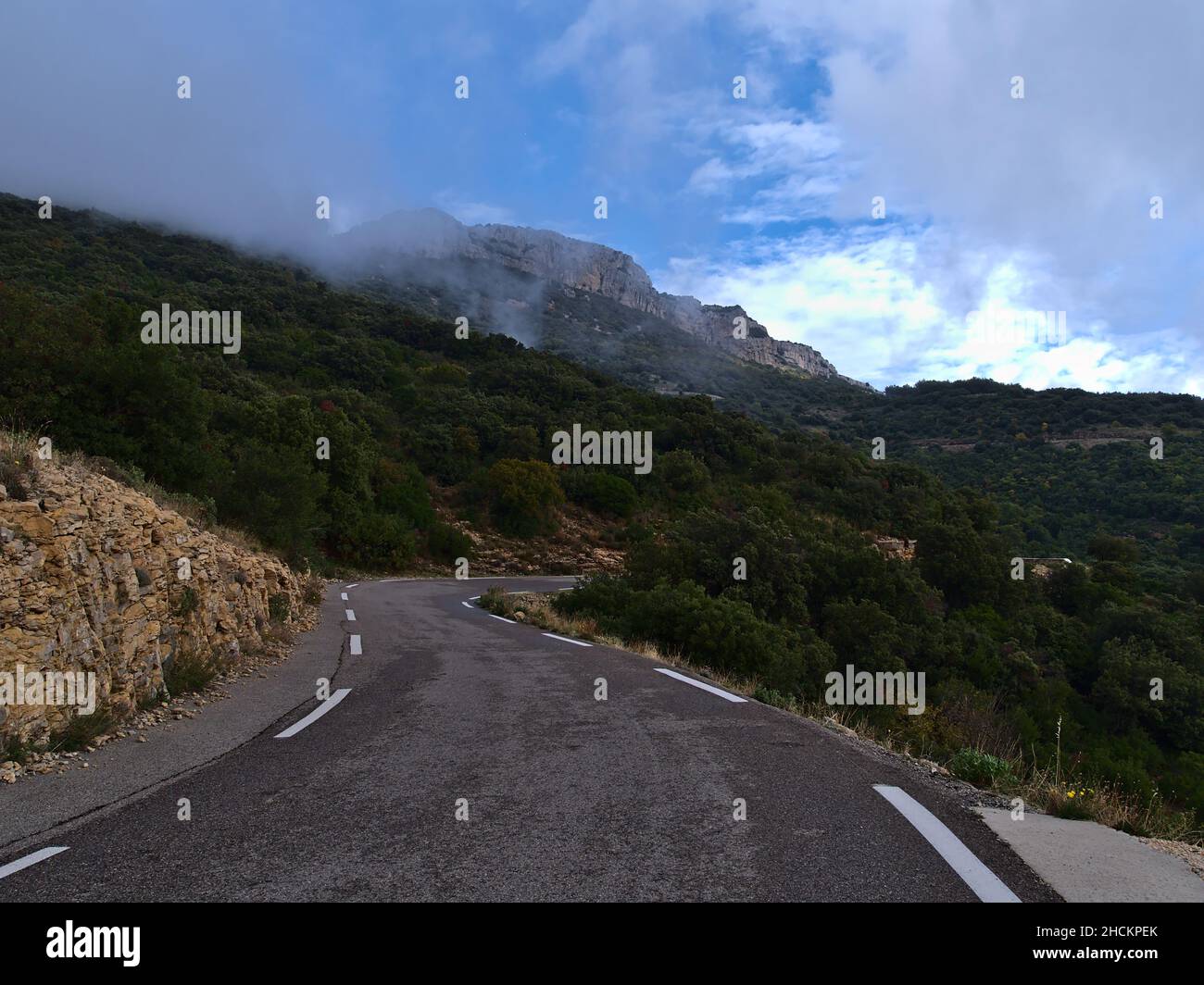 View of curvy mountain road D2 in Massif de la Sainte-Baume in Provence, France on cloudy day in autumn surrounded by forest. Stock Photo