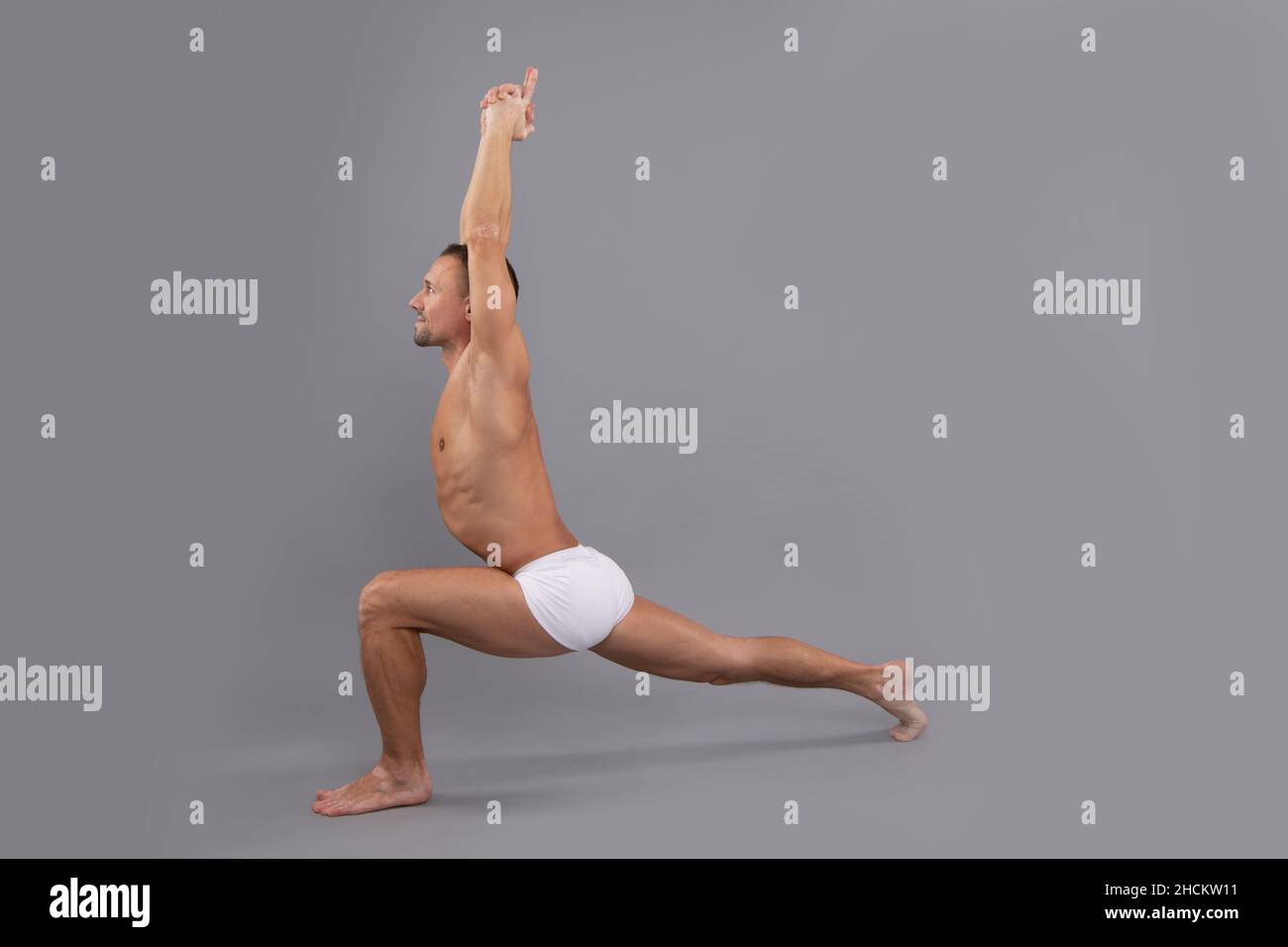 Pilates for every body. Fit guy do crescent lunge greybackground. Yoga and pilates exercise Stock Photo