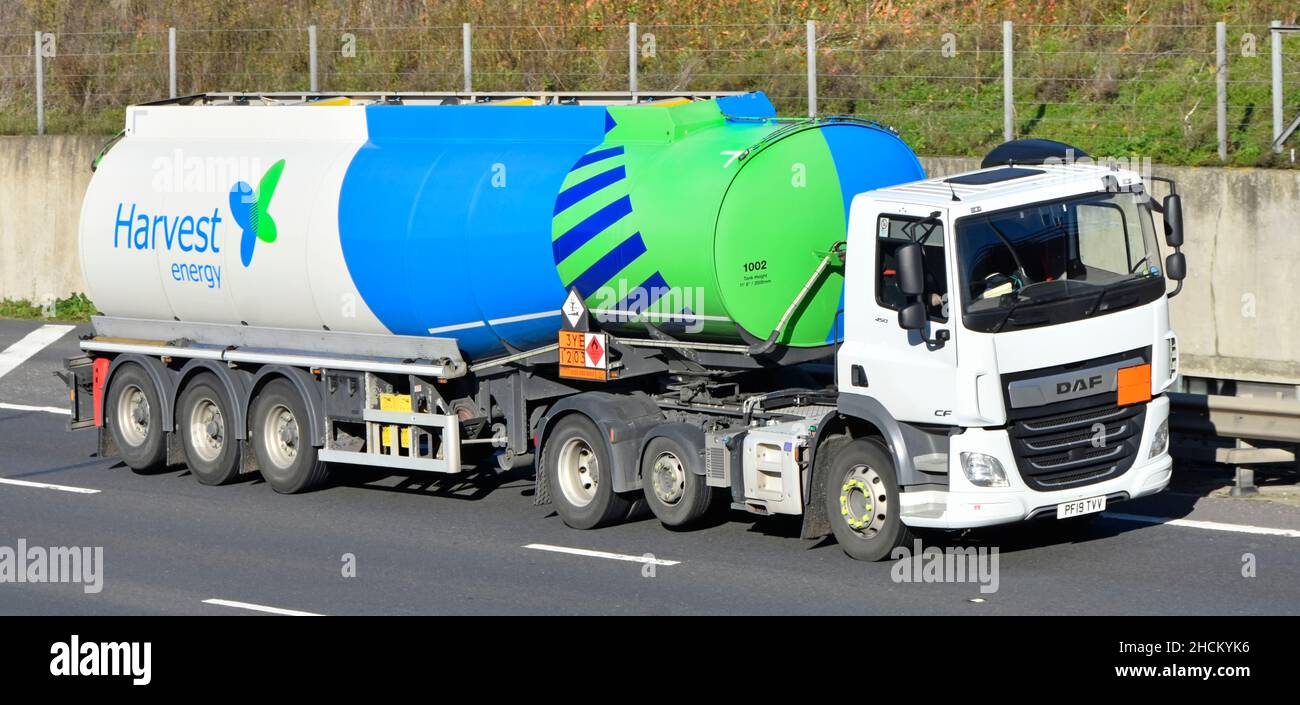 Harvest Energy colourful articulated fuel delivery tanker trailer & brand logo white DAF lorry truck hgv drivers cab driving along on UK motorway road Stock Photo