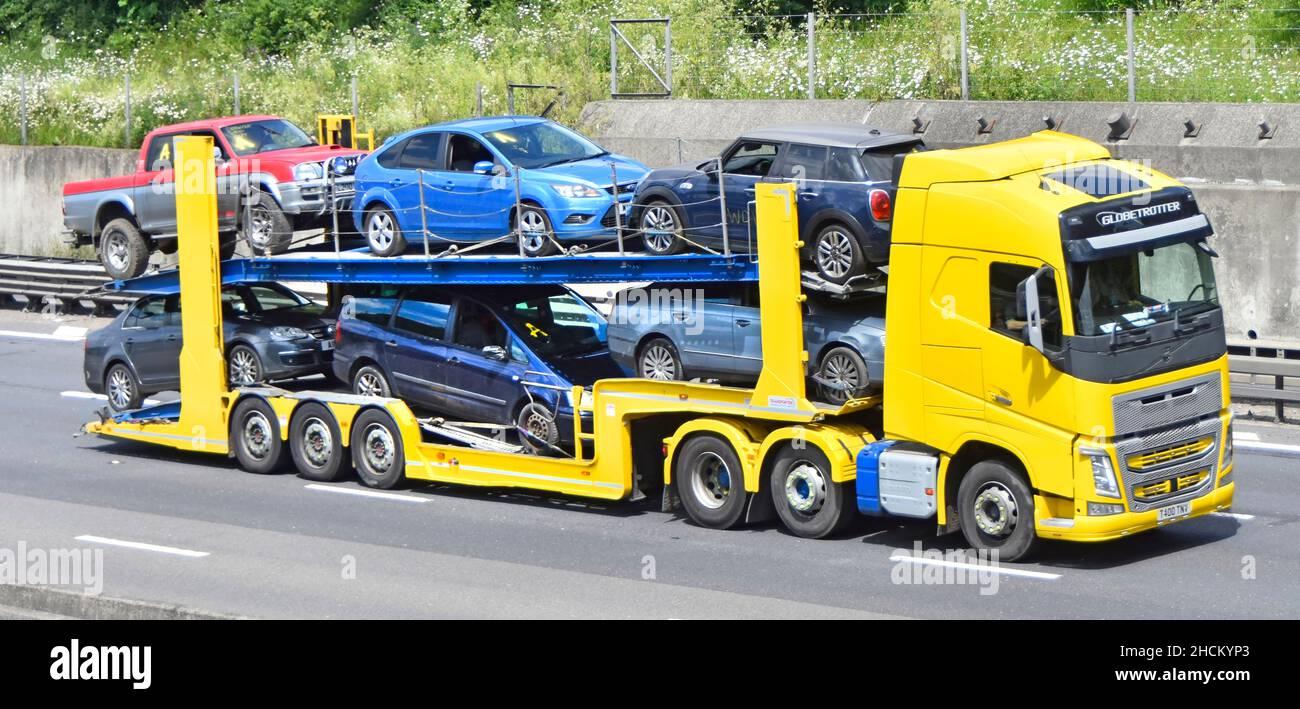 Side & front view yellow hgv lorry truck driver articulated car transporter loaded assorted secondhand cars & pickup truck driving along UK motorway Stock Photo