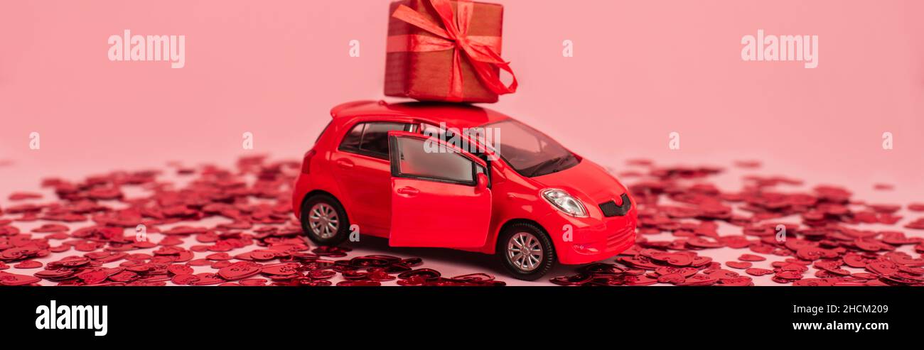 toy car with wrapped present near shiny red confetti hearts isolated on pink, banner Stock Photo