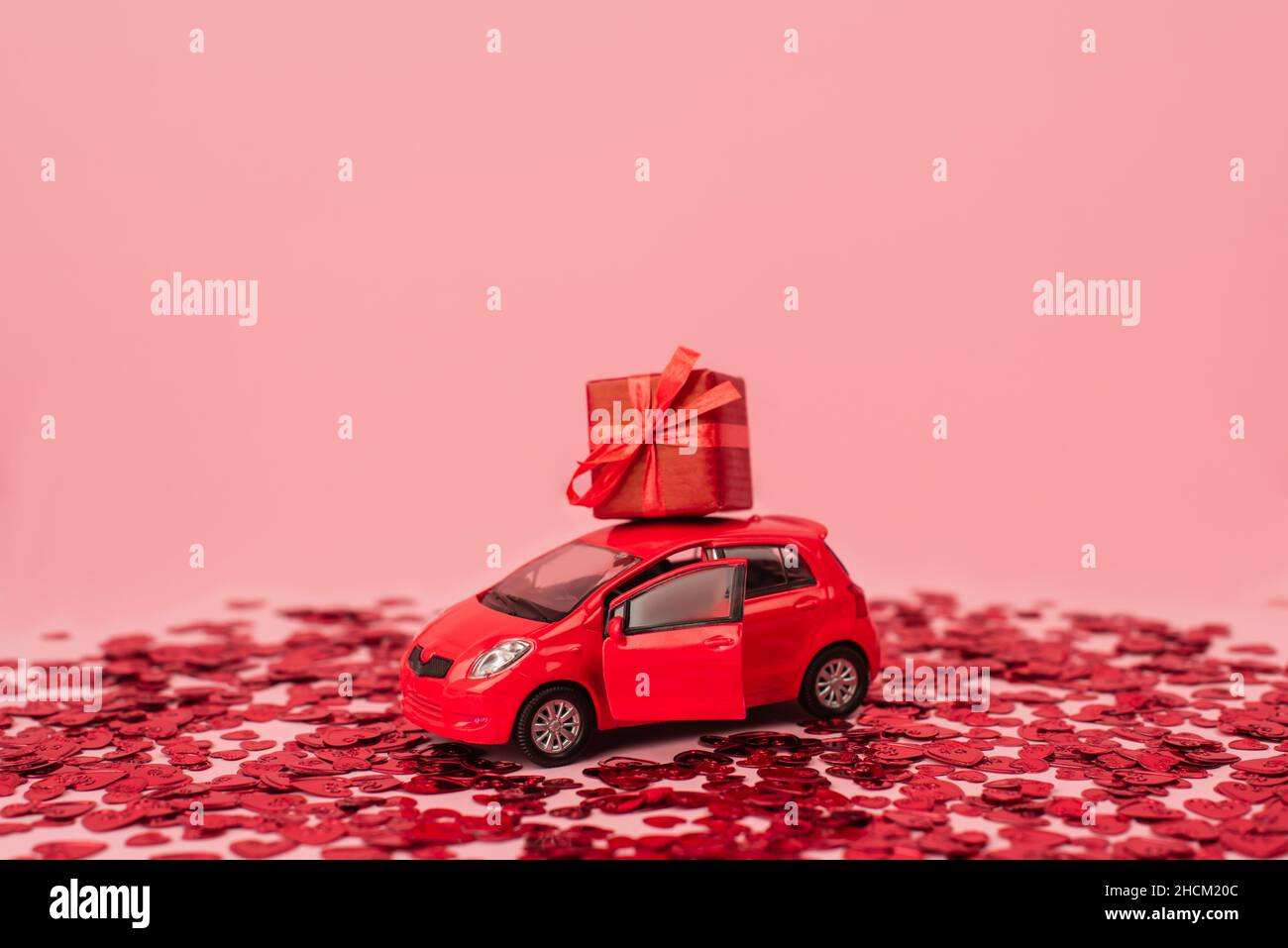 toy car with wrapped present near shiny red confetti hearts isolated on pink Stock Photo