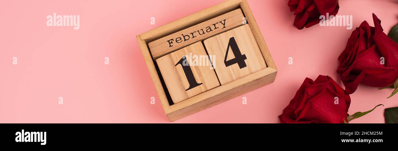 top view of red roses near calendar with 14 february lettering on pink ...