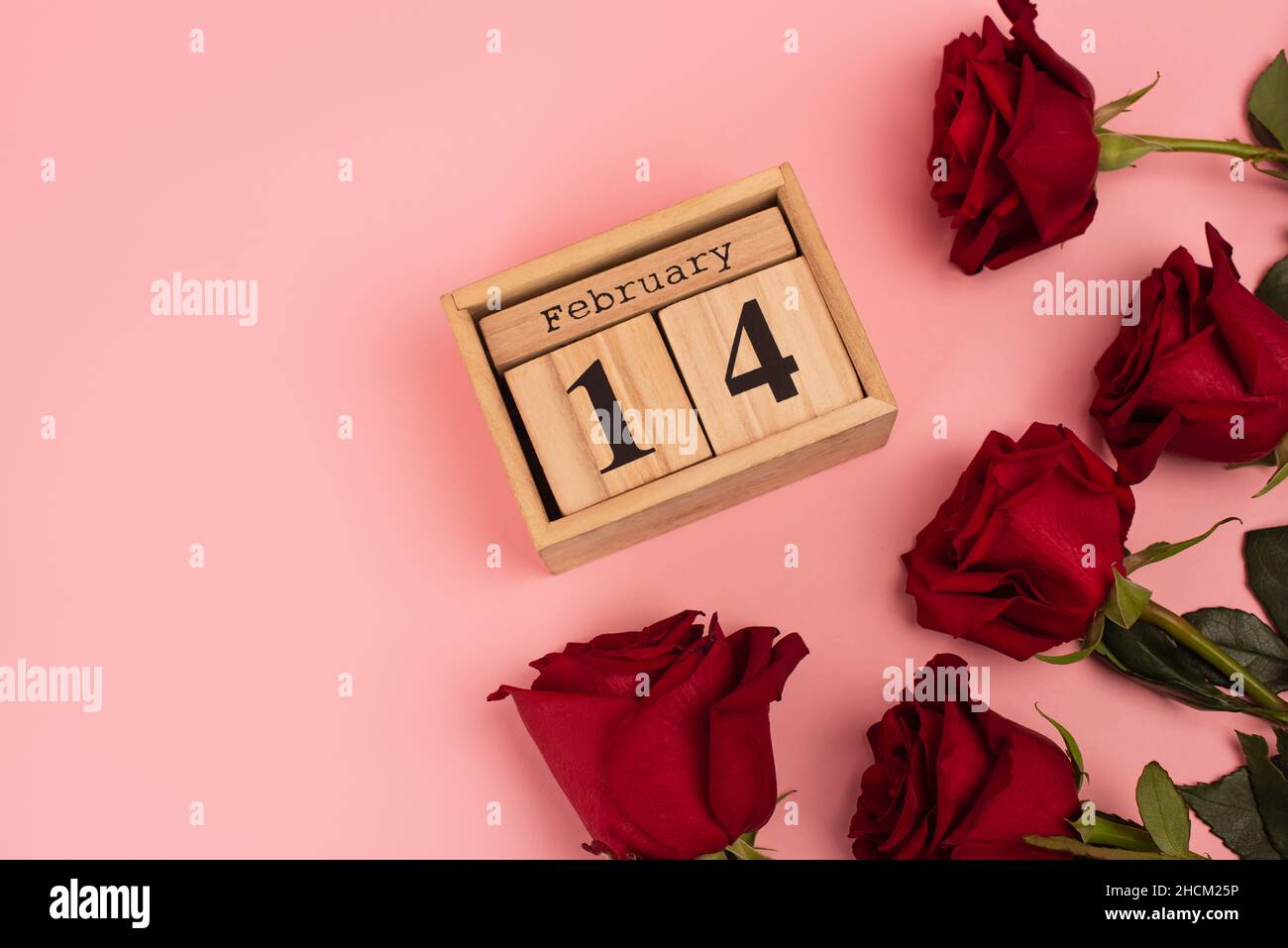 top view of red roses near calendar with 14 february lettering on pink ...