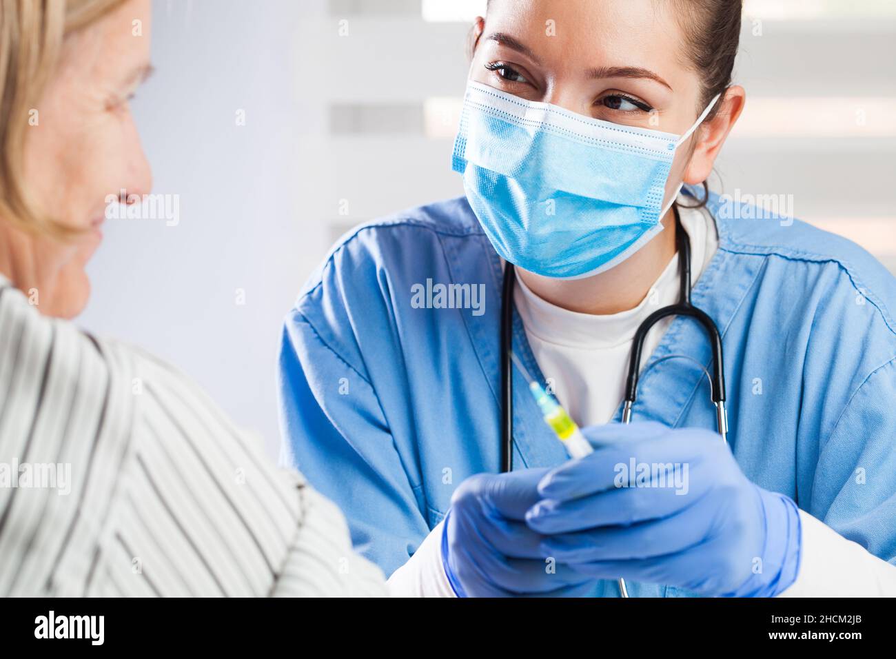 Young female caucasian medical NHS worker giving coronavirus injection shot to elderly woman patient,immunization against COVID-19 virus disease,boost Stock Photo
