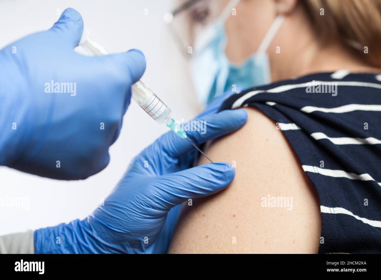 Closeup of medical worker's hands in blue protective gloves injecting vaccine booster shot into elderly patient's shoulder,Coronavirus vaccination Stock Photo