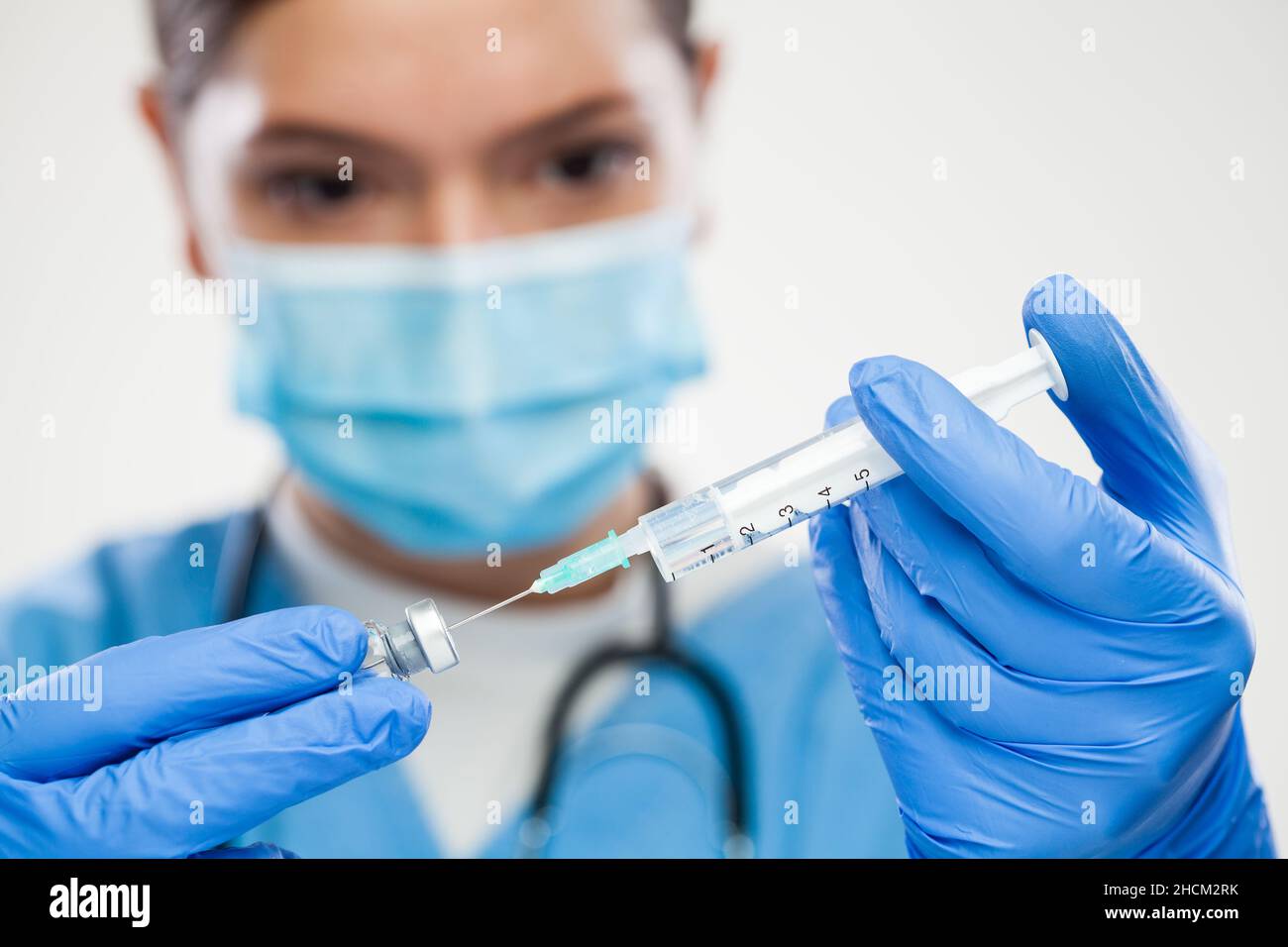 Female medical NHS worker taking vaccine shot dose from glass ampoule,needle in vial filling syringe,process of preparation for Coronavirus vaccine Stock Photo
