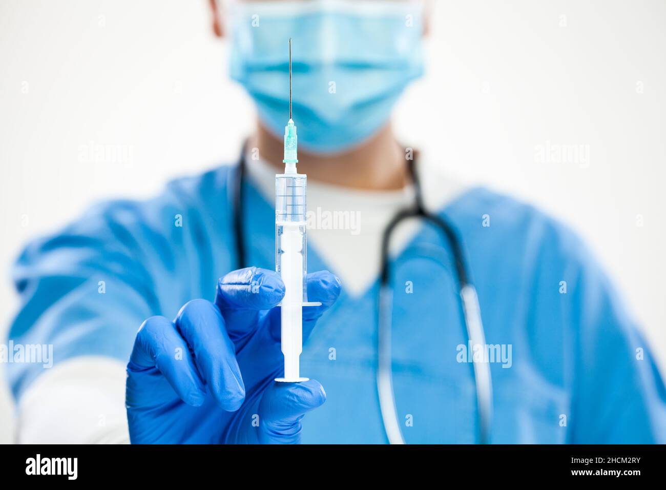 Closeup of syringe in needle with vaccination dose,medical worker wearing blue protective surgical face mask,latex gloves scrubs,vaccination Stock Photo