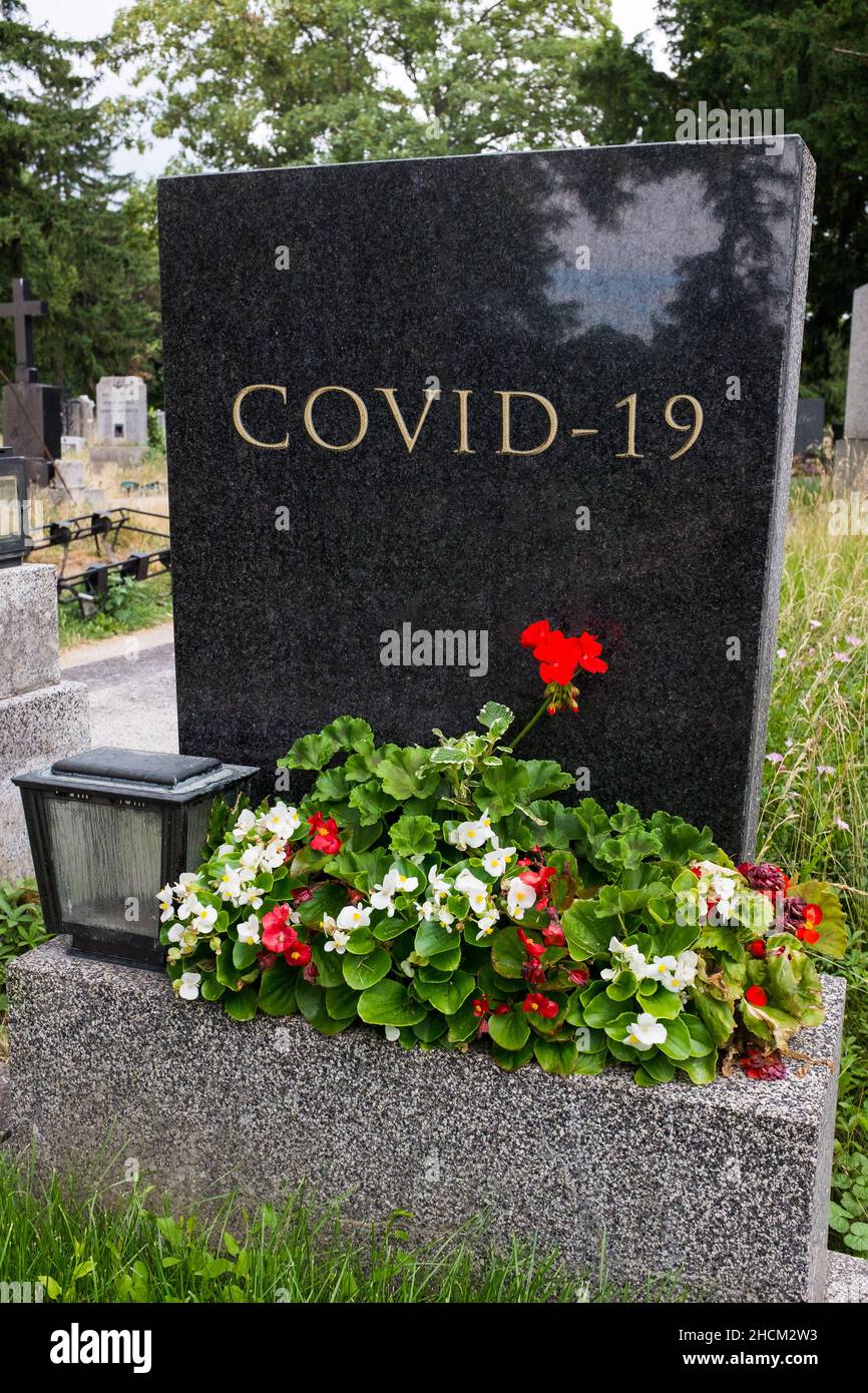 Black granite or marble tombstone with flowers and COVID-19 inscription,concept of Coronavirus virus disease victims,high mortality rate and death Stock Photo