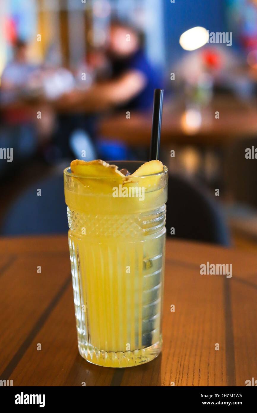 Glassy glass stands on table with drinking straw, which been poured tea, lemonade with lemon and ginger. Stock Photo