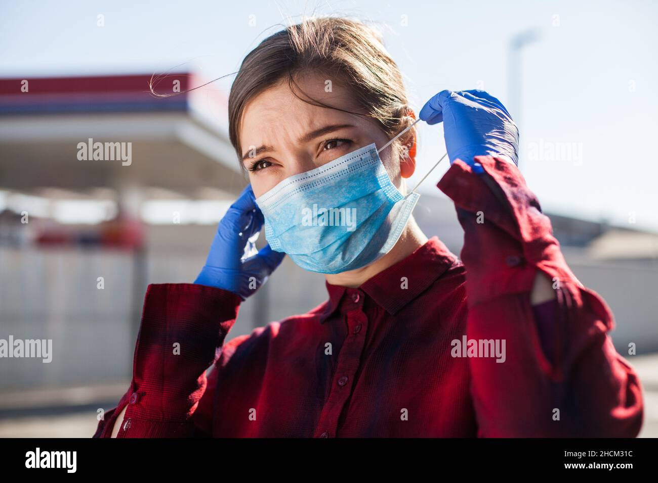 Young pretty caucasian woman putting protective face mask on,worried concerned expression,Coronavirus pandemic crisis prevention protection measures Stock Photo
