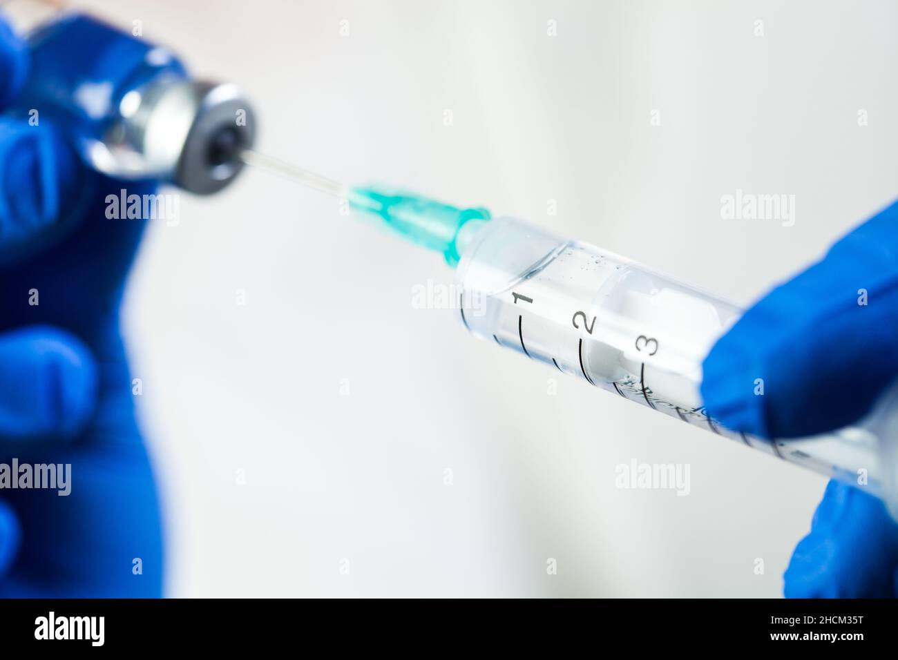 Macro closeup of syringe with needle in ampoule vial,details of blue latex gloves holding vaccination equipment,COVID-19 immunization procedure Stock Photo