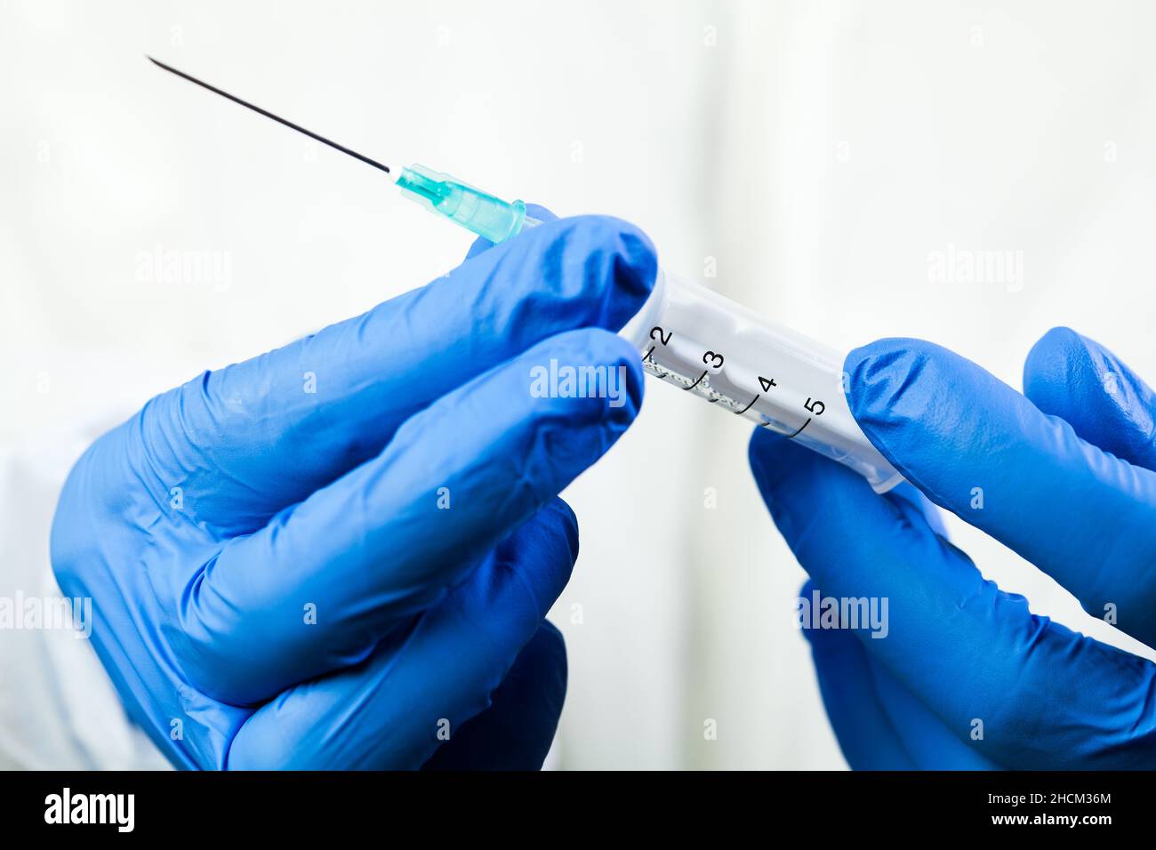 Closeup of hands in blue gloves holding syringe with needle full of vaccination shot dose,COVID-19 immunization procedure,medical worker in NHS health Stock Photo