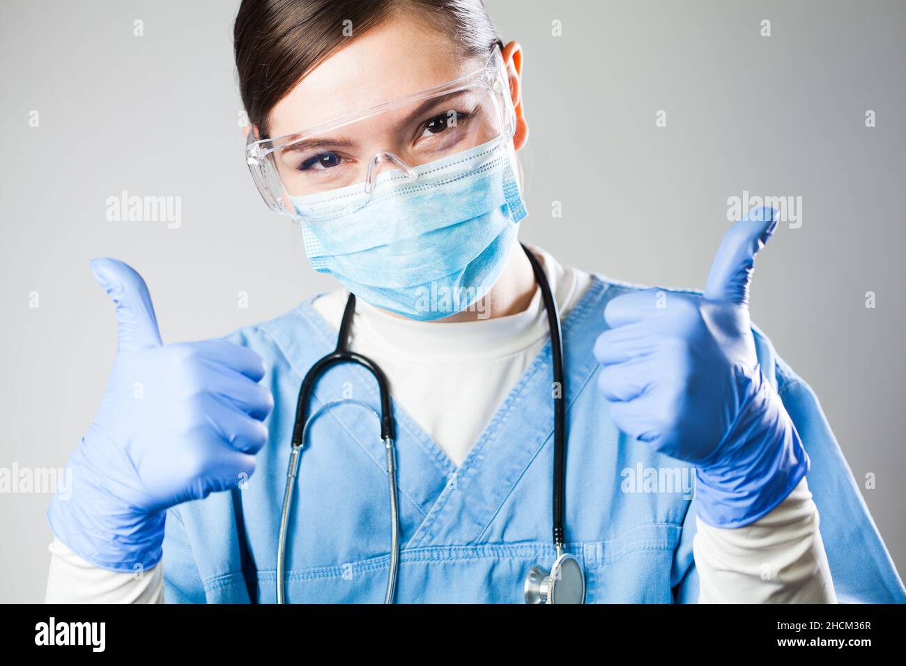Pretty caucasian female doctor,cheerful,optimistic and positive medical worker holding both thumbs up,successful patient therapy and treatment Stock Photo