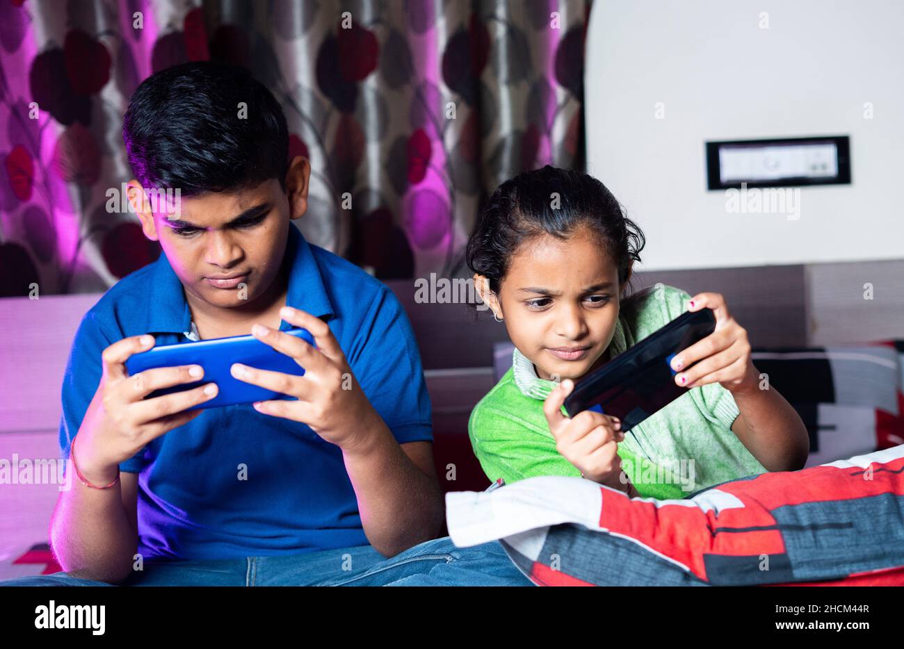 Siblings busy playing video game on mobile phone during night sleep - concept of kids gaming addiction, childhood lifestyles and technology. Stock Photo