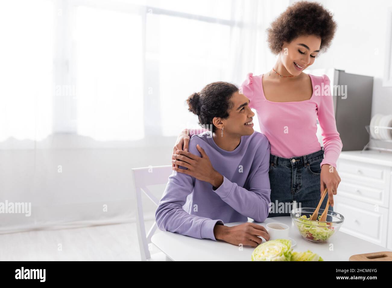 African american woman hugging boyfriend and cooking salad in kitchen ...