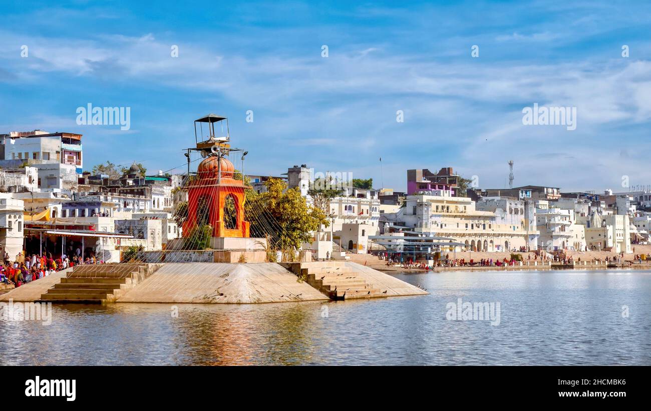 An orange monument on an artificial island in Pushkar Lake, a site sacred to Hindu pilgrims who visit the ghats to bathe in its holy waters, in Rajast Stock Photo