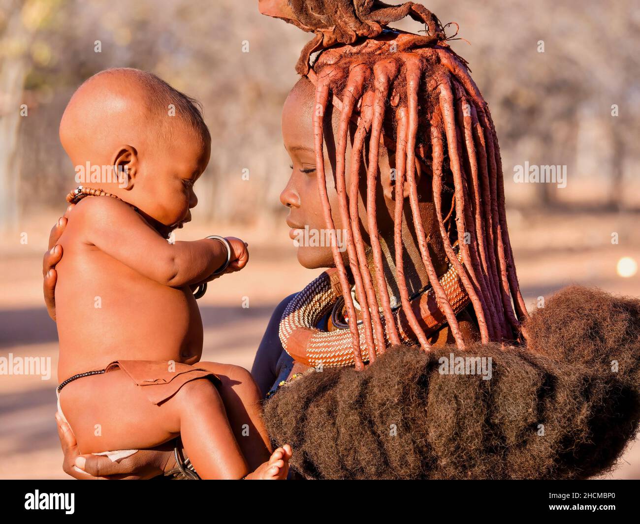 Palmwag, Namibia - August 21, 2016. A young African woman holds her baby while wearing the traditional hairstyle and ochre skin paste of the Himba tri Stock Photo