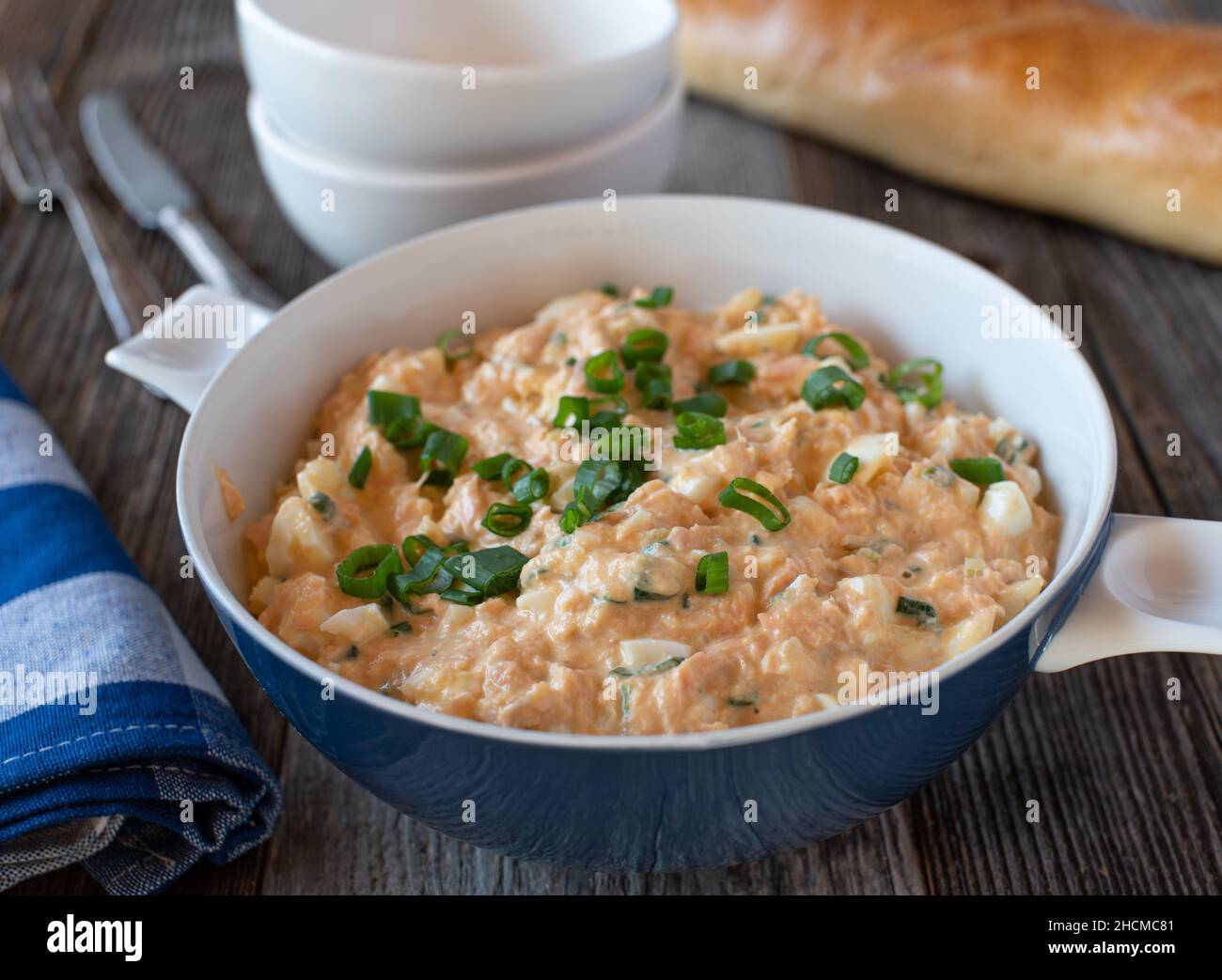 Seafood salad in a bowl made with salmon fillet, boiled eggs, onions, mayonnaise and chives. Served with fresh baguette on wooden table Stock Photo