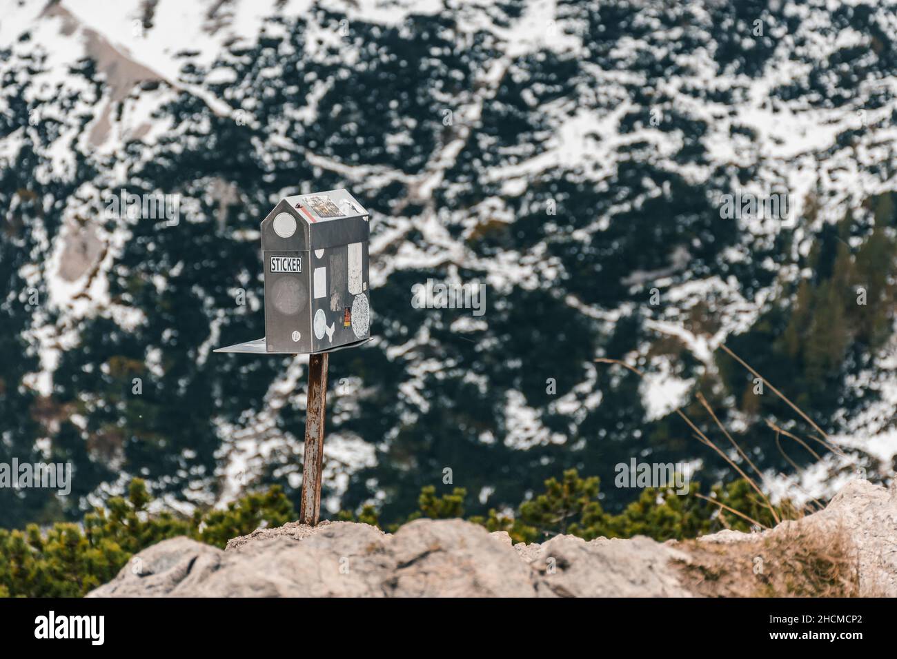Closeup of a metal box with hiking passbook stamps on a rock against mountains covered with snow Stock Photo