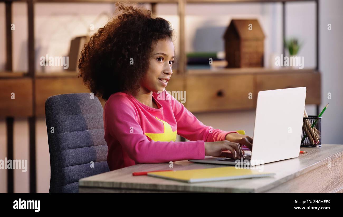 cheerful african american schoolkid using laptop while doing homework ...