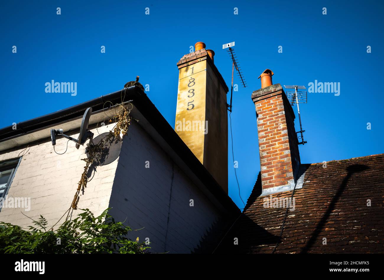 Chimneys with TV aerials on old houses in Billingshurst, West Sussex, UK. One chmney is marked with the number 1835 to show the year it was built. Stock Photo