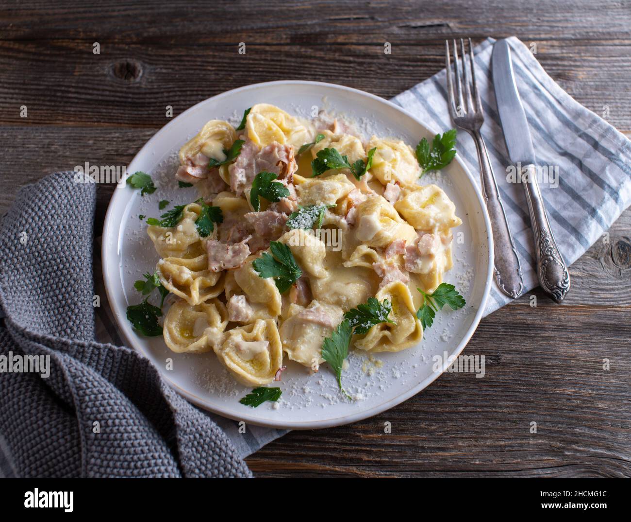 Tortellini alla panna. Traditional fresh cooked italian pasta dish. Served on a white plate isolated on wooden table background Stock Photo