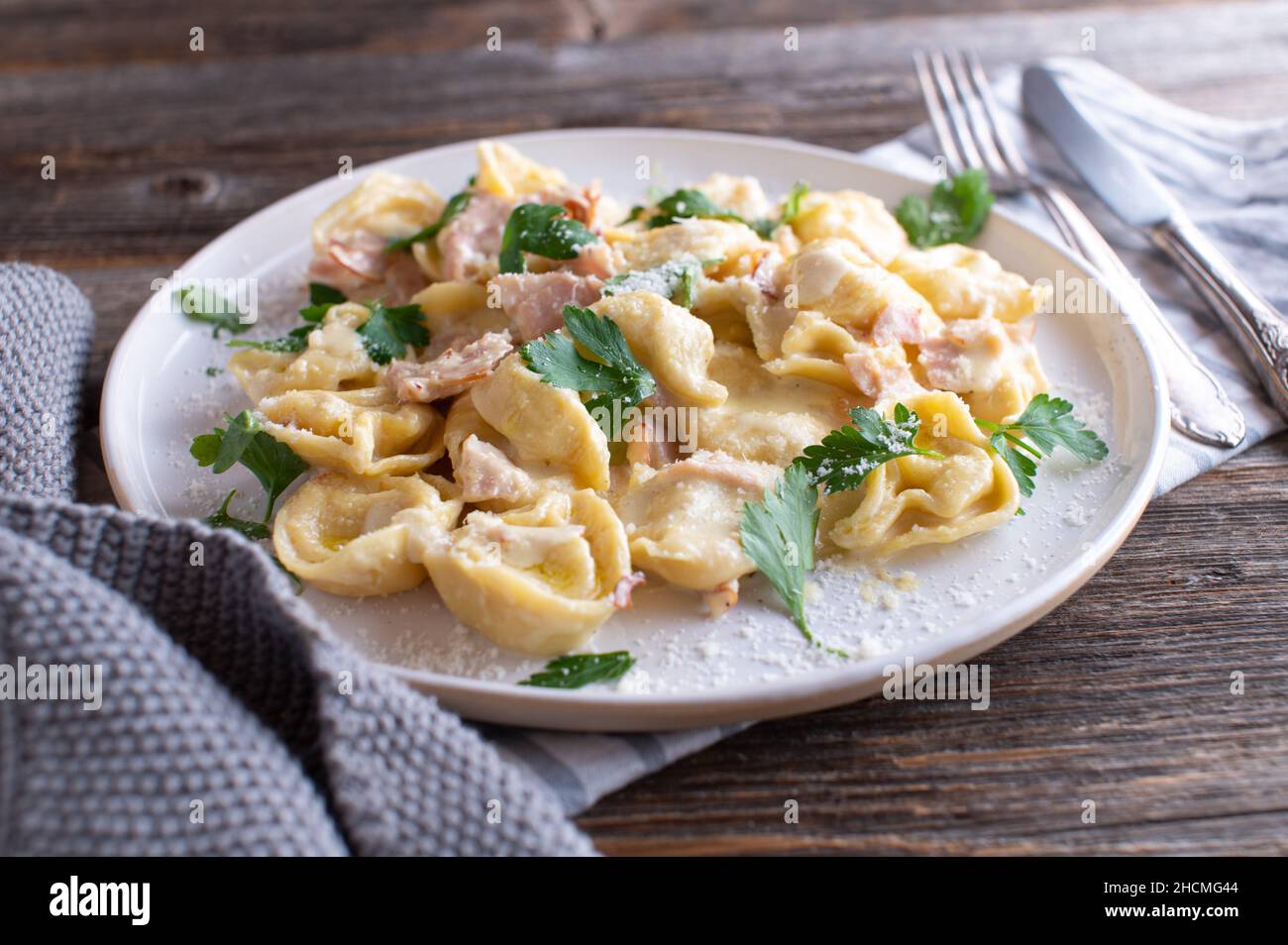 Tortellini alla panna. Traditional fresh cooked italian pasta dish. Served on a white plate isolated on wooden table background Stock Photo