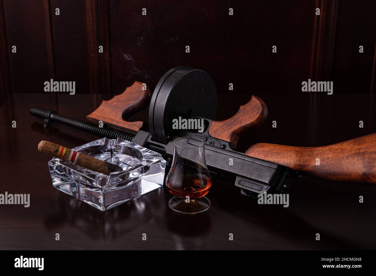 Vintage Thompson submachine gun on a dark brown table with a cigar and whiskey  Stock Photo
