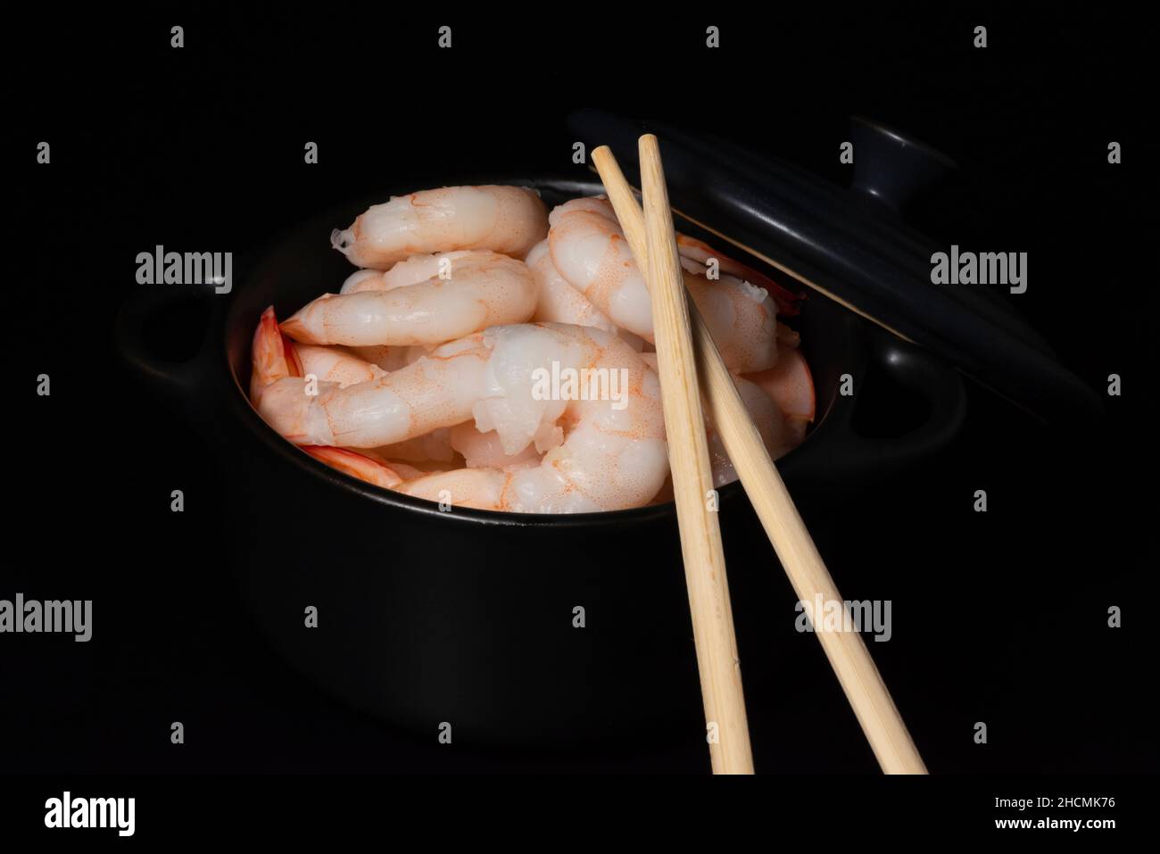Contrast view of cooked prawns and chopsticks in bowl on black background. Stock Photo