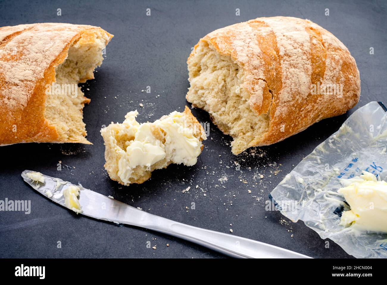 Buttered Piece of Freshly Baked Baguette: French bread with butter on a dark background Stock Photo