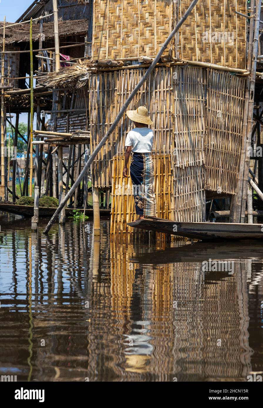 Ethnic minority Intha woman in small boat outside stilt house on Ethnic minority Intha woman in small boat outside stilt house on Inle Lake,Shan State Stock Photo