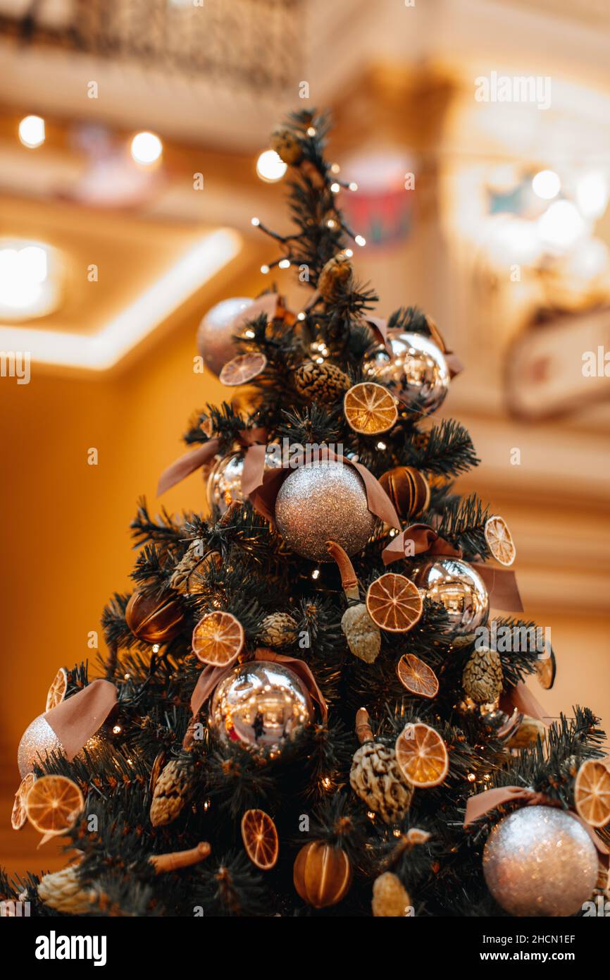 Creative interesting Christmas tree decorated with dried oranges, mandarins, pine cones and golden glittering Christmas balls. Magic details. Winter s Stock Photo