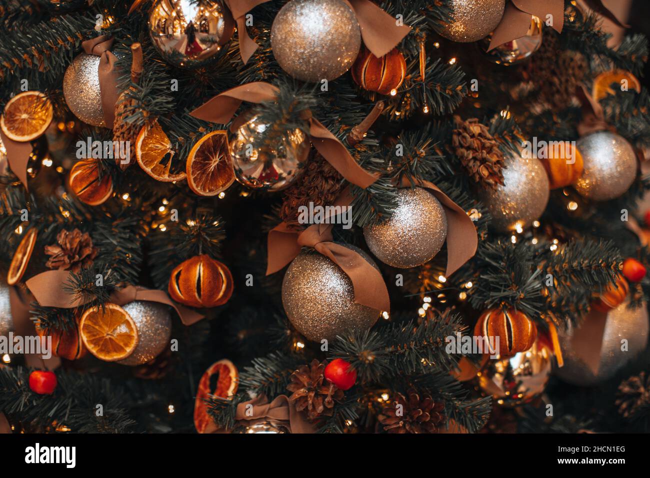 Dried mandarins, oranges, pine cones Christmas balls hanging on the Christmas tree branches. Cozy winter details and golden magic bokeh lights. Winter Stock Photo