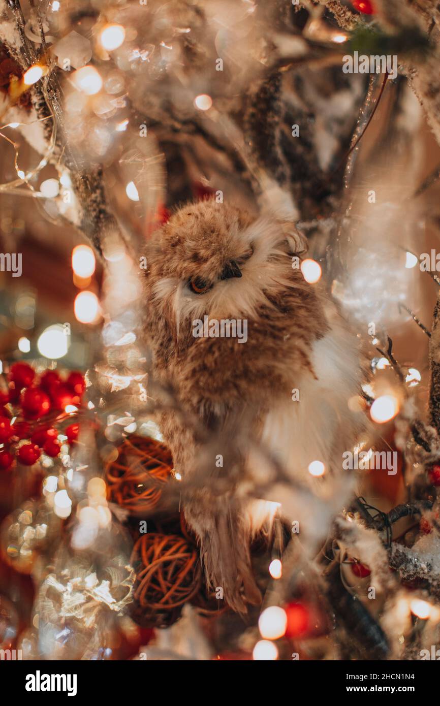 Fluffy beige figurine of an owl on silver sparkling branches with golden bokeh garlands. Christmas and New Year festive decoration Stock Photo