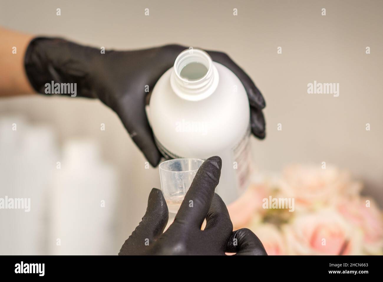 A hairdresser in black gloves is preparing hair dye with a bottle in a