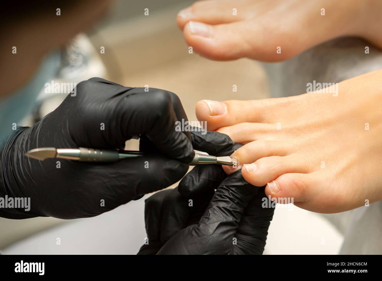 Cuticle Removal on Toes. Hands in black gloves of pedicure master