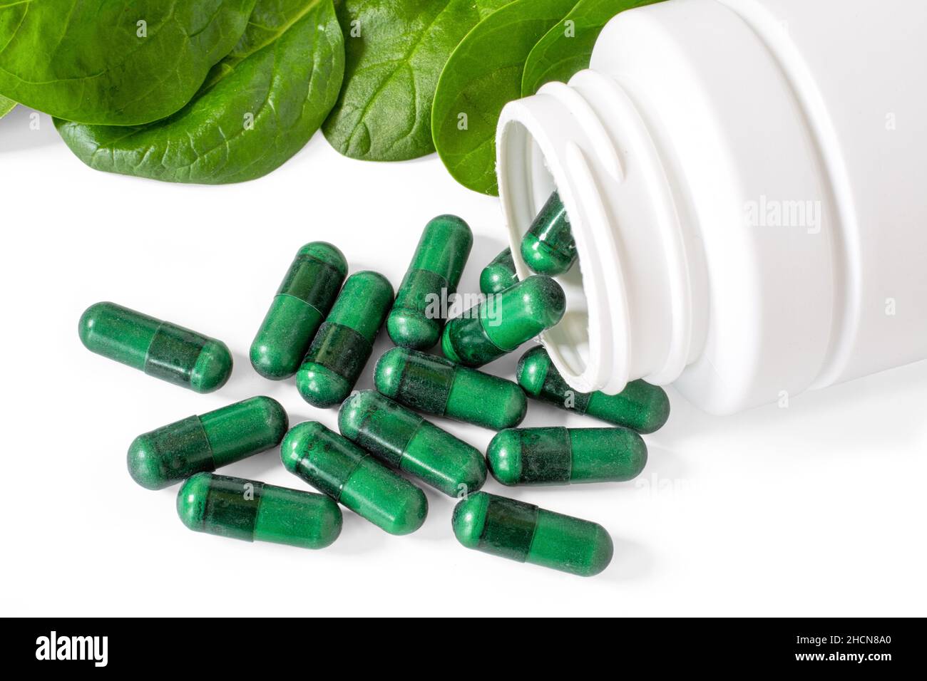 Green supplement capsules with spinach leaves on white. Stock Photo
