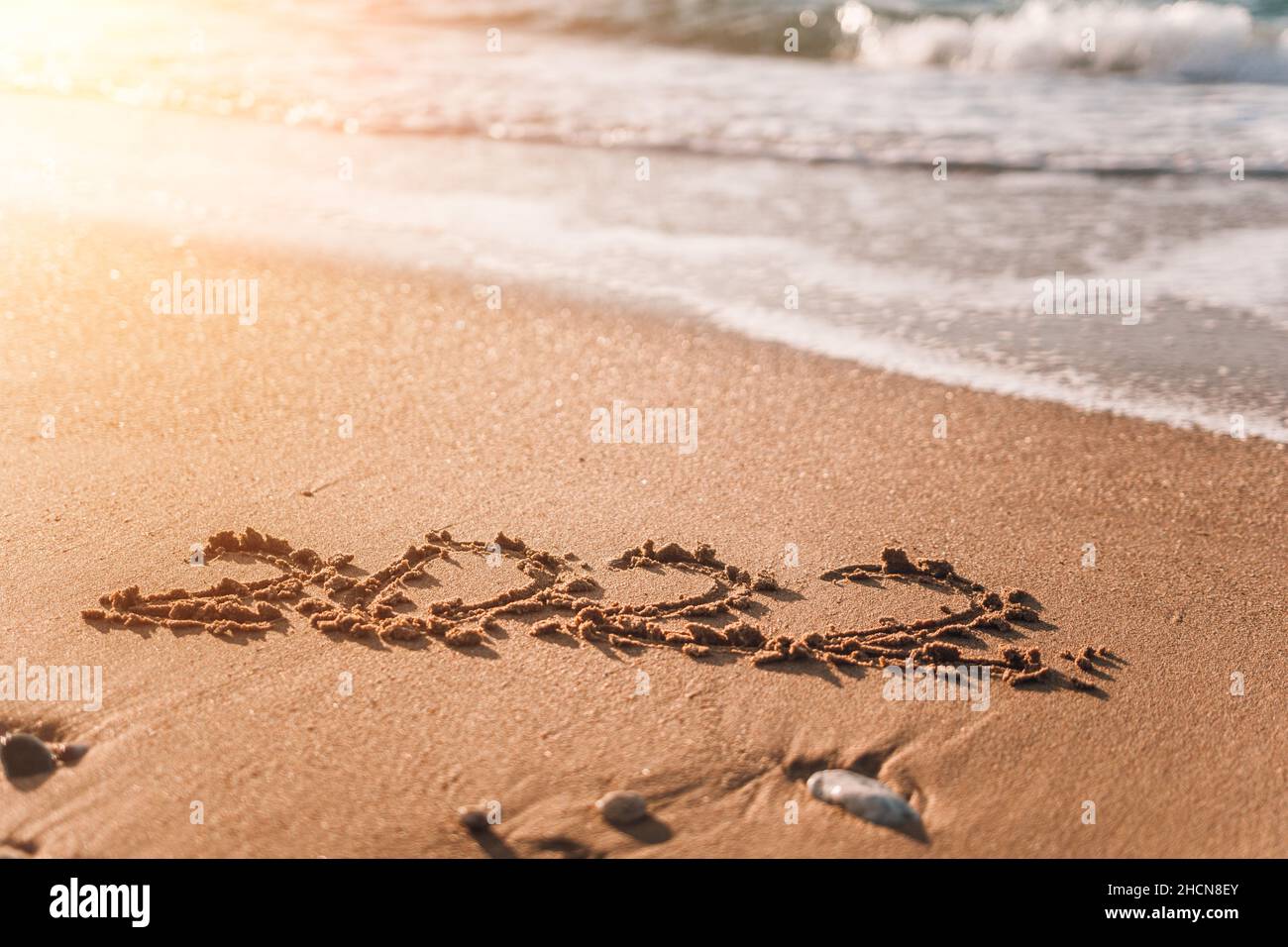 2022 figures on sandy beach Happy New Year 2022, number hand written in the golden sand on beautiful sunset golden light. The sea wave washes away the Stock Photo