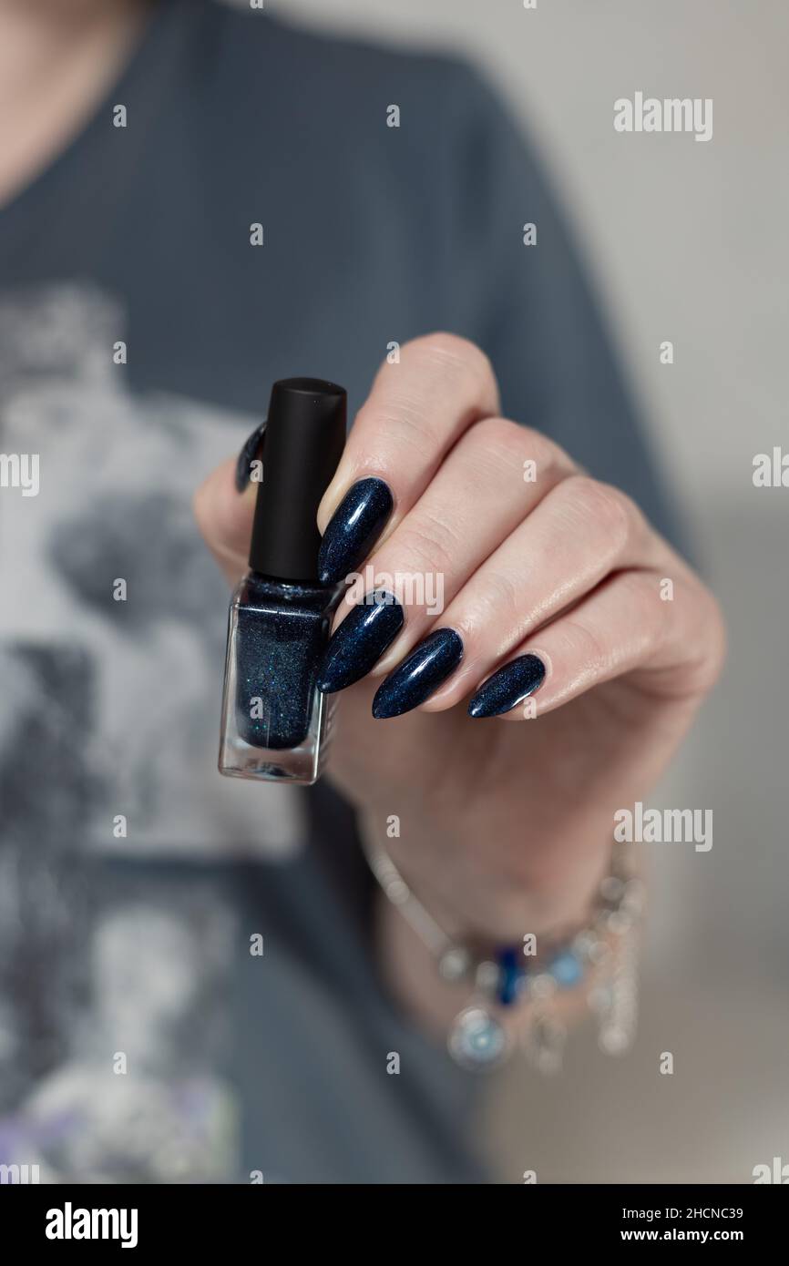 Female hand with long nails and dark blue teal manicure holds a bottle of  nail polish Stock Photo - Alamy