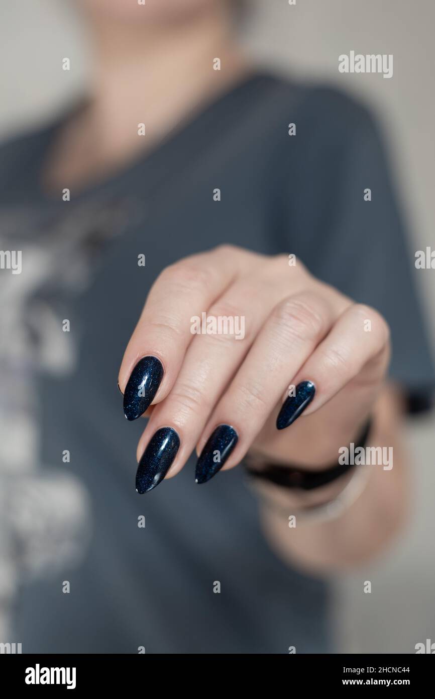 Female hand with long nails and dark blue teal manicure holds a bottle of  nail polish Stock Photo - Alamy