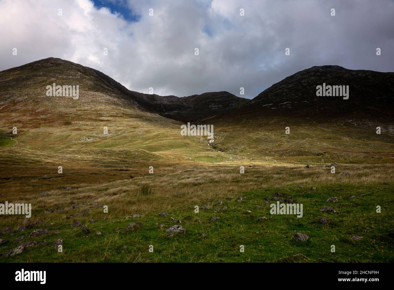 Green sloping mountains and a waterfall near Maumeen pass in National Park Connemara in county Galway in Ireland Stock Photo